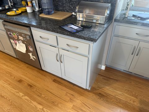 Cabinet painting, light grey lower cabinets beside dishwasher, granite counter, oak floor, kitchen, Elements Painting project on the Colorado Front Range