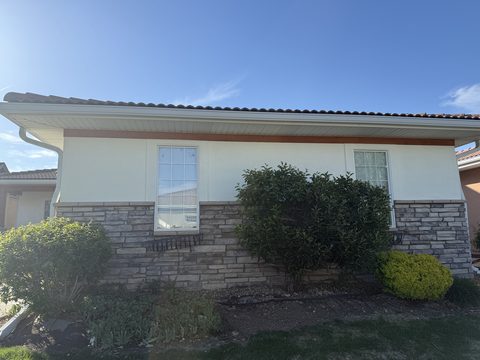 Exterior painting, cream stucco wall, stone base, white trim, shrubs, Elements Painting project on the Colorado Front Range