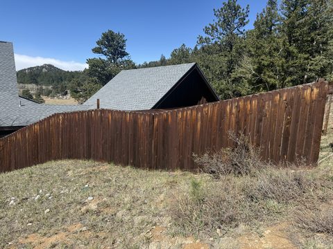 Deck and fence staining, dark brown stained wood privacy fence, grey-roofed house behind, Elements Painting project on the Colorado Front Range
