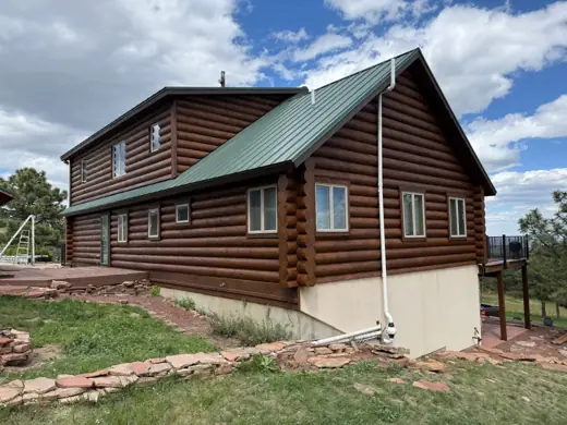 Freshly stained log home with green metal roof and stone base, Elements Painting project on the Colorado Front Range