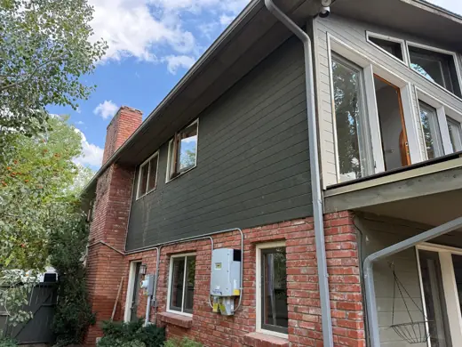 Gray-green house with red brick base and mature trees, Elements Painting project on the Colorado Front Range