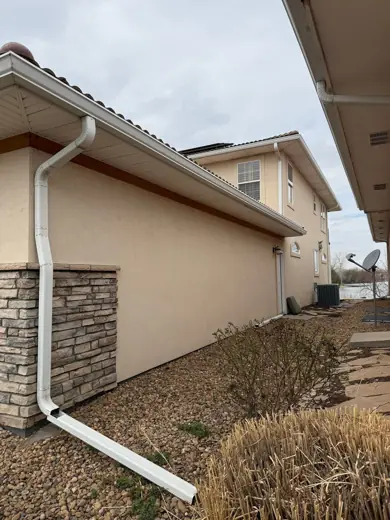 White stucco home side with stone accents and downspout, Elements Painting project on the Colorado Front Range