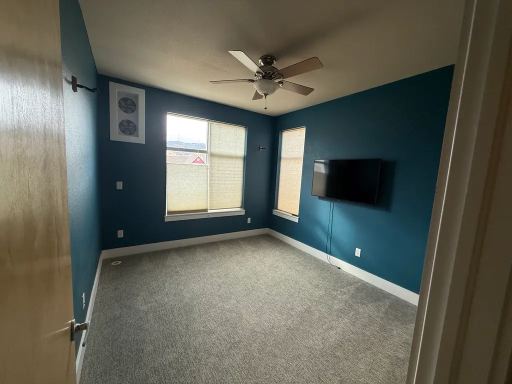 Bedroom Interior Painting with Teal Blue Walls Newly painted bedroom featuring vibrant teal blue walls, light gray carpet, ceiling fan, and windows.